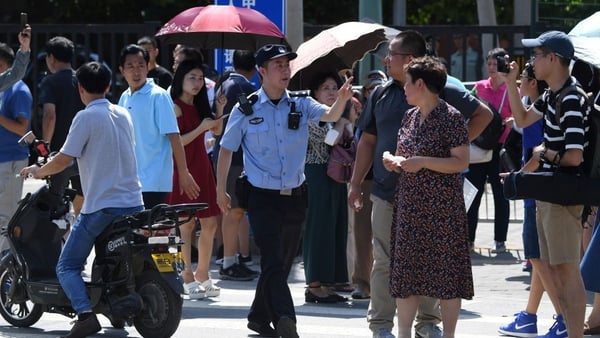 A Chinese police officer gestures among a crowd of bystanders gathered outside the US embassy in Beijing following a blast