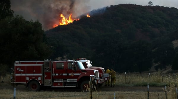 Firefighters look on as the River Fire burns through a canyon in Lakeport, California