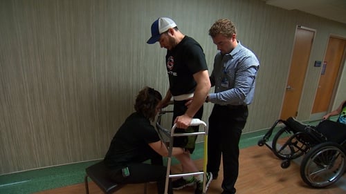 Jered Chinnock taking steps with a front-wheeled walker while trainers provide occasional assistance (Pic: Mayo Clinic)