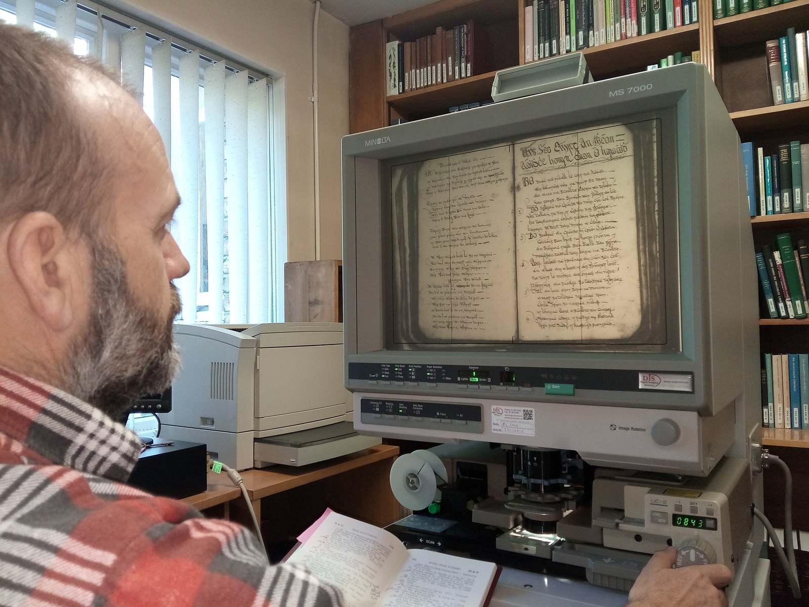 Image - An tOllamh Brian Ó Curnáin ag scrúdú lámhscríbhinn Éamainn Uí Orchaidh ar mhicreascannán