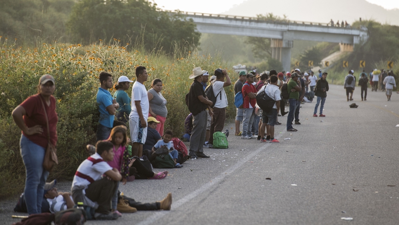 Migrants travelling towards the United States taking a rest along a road, hoping to hitch a ride on a passing vehicle