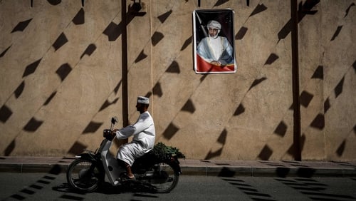 A man rides a motorcycle past a wall bearing a portrait of Oman's Sultan Qaboos. Photo: Philippe Lopez/AFP/Getty Images