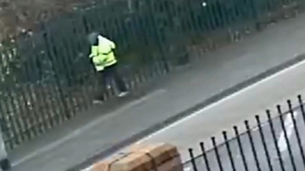Security camera material shows a man in a high-visibility coat walking near a school