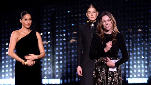 Clare Waight Keller is watched by Meghan and Rosamund Pike as she speaks on stage after receiving the award for British Designer of the Year Womenswear Award