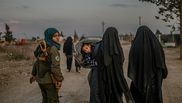 Wives of IS fighters walk under the supervision of a female fighter from the SDF in northeastern Syria