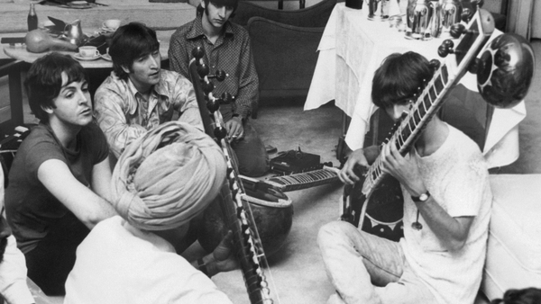 Beatle George Harrison receiving instruction in playing the sitar from a Sikh teacher as the other members of the Beatles look on in quiet fascination