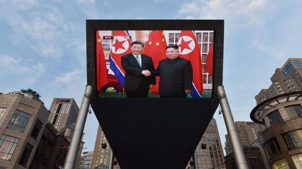 News footage of Xi Jinping (L) being greeted in Pyongyang by Kim Jong-un is shown on a large screen outside a shopping mall in Beijing