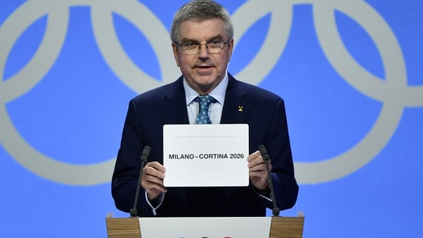 IOC president Thomas Bach shows the card with the name Milan