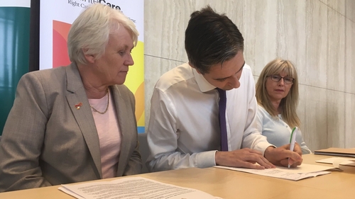 Minister of State Catherine Byrne (L) watches as Simon Harris signs the legislation