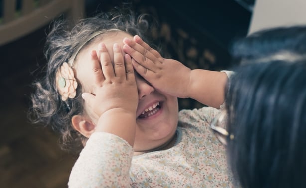 Happy little girl playing peekaboo game with mother and covering her eyes with hands
