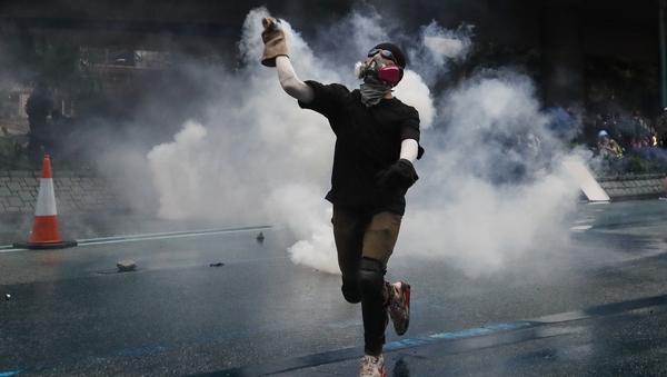 A protester wearing a gas mask throws back a tear gas after police fired tear gas during an anti-government rally