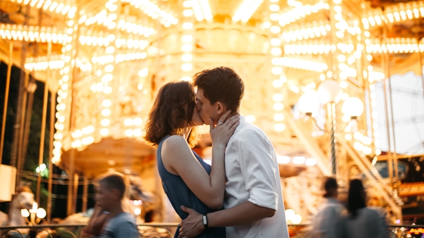 Caucasian couple kissing in front of carousel