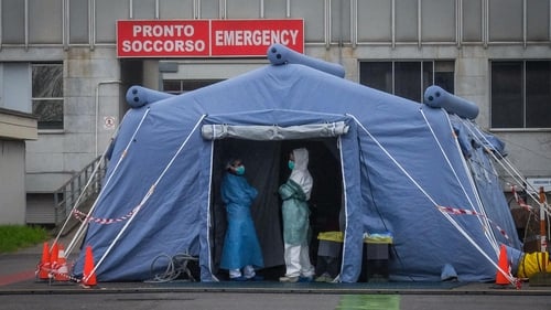 Health workers wearing protective suits and masks stand at the entrance of an advanced medical unit built in front of the Cremona Hospital