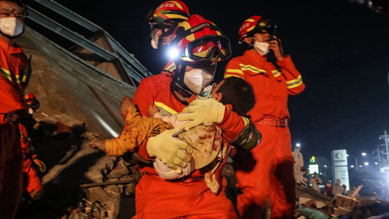 A boy is rescued from the rubble by a firefighter wearing a protective face mask