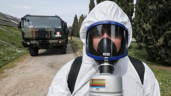 An Italian soldier wearing a protective suit helps in the transportation of coffins on military trucks from the Bergamo area