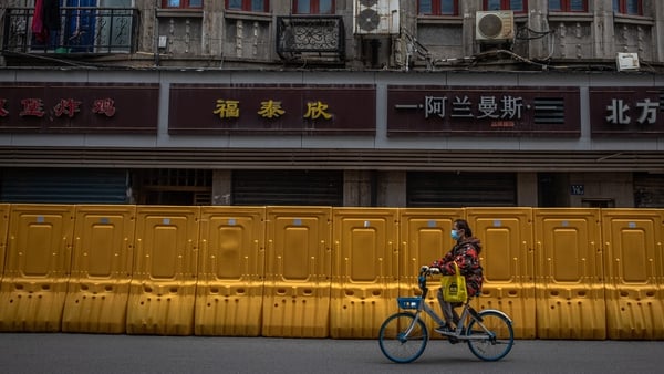 A woman wearing a protective face mask rides a bicycle on a road next to a security fence separating a residential area and a street, in Wuhan