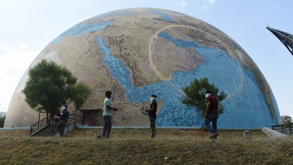 Staff members of the the Gujarat Science City wearing face-masks stand in front of a planet earth model