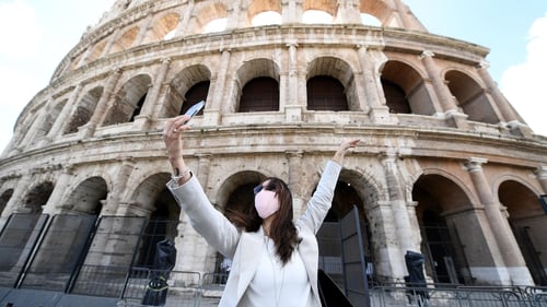 A woman wearing a protective mask takes selfie photos in front of the Colosseum in Rome
