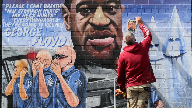 Artist Mickey Docherty removes a photo used to paint a mural of George Floyd in Belfast