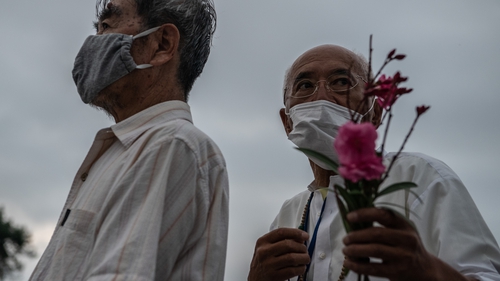 A man holds a flower as he queues to pray in remembrance of the victims of the Hiroshima bombing