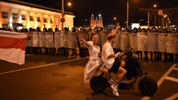 A couple rides a scooter in front of riot police during a protest after polls closed in Belarus' presidential election