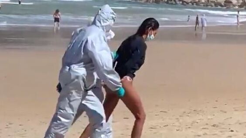 Gloved
          officers in white hazmat suits marched the handcuffed woman
          off the beach in the northern city of San Sebastian (Pic:
          @JavierSanz)