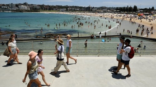 People commute on a walkway as others cool off in the water during heatwave conditions at Bondi Beach in Sydney