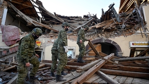 Croatian soldiers walk on wreckage next to damaged buildings in Petrinja