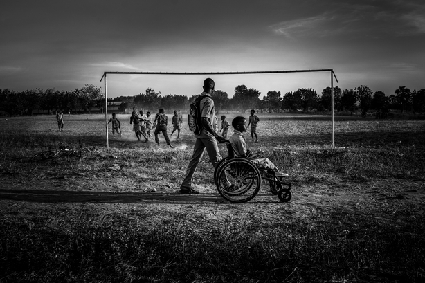 A child eing pushed in a wheelchair against a backdrop of others playing football