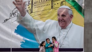 Young girls take a selfie in front of a poster promoting the upcoming trip of Pope Francis in Erbil