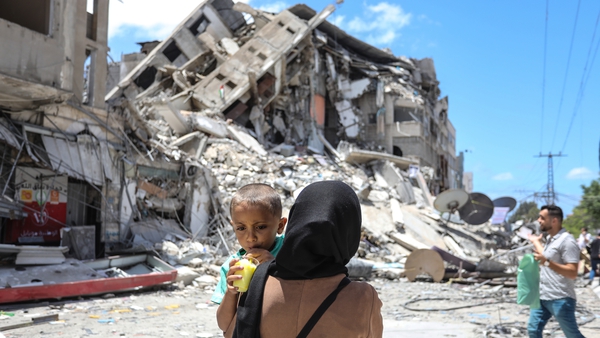 A Palestinian woman carries her baby near the rubble of Al Shorouq tower in Gaza