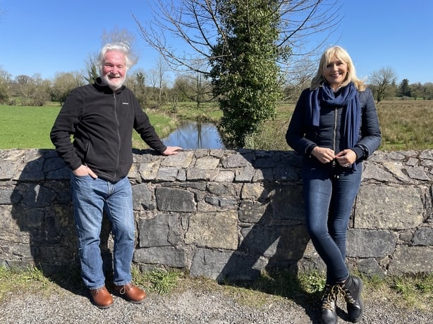 Miriam stands by a wall with darach MacDonald
