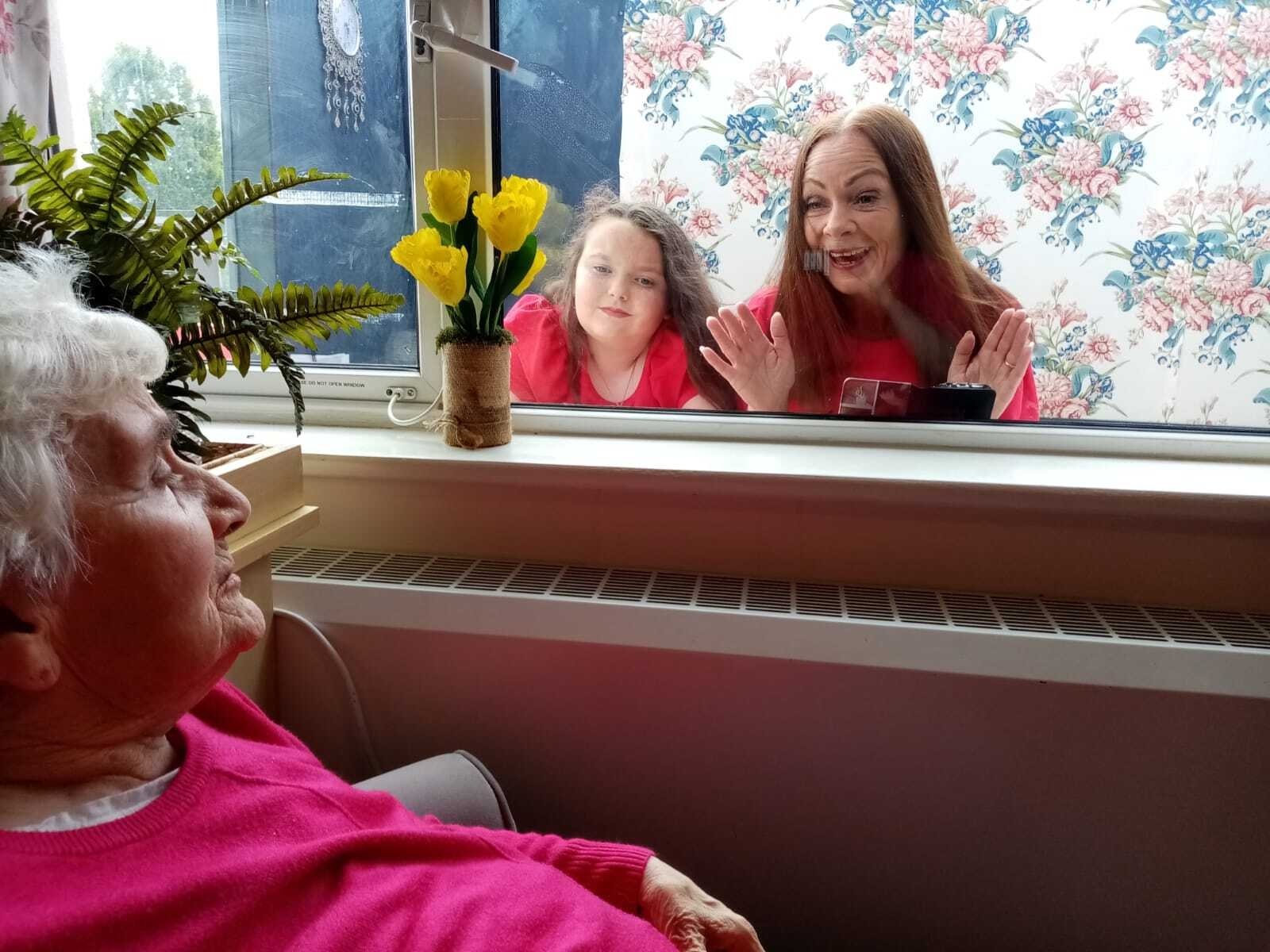 Image - Christine Thompson and her daughter, Sarah, enjoy a precious window visit with her mother, Kathleen