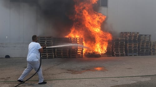 A municipal worker sprays water on burning pallets during a bushfire near Athens today