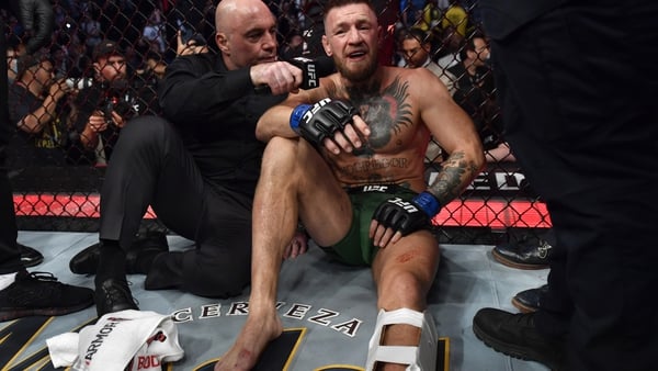 Conor McGregor (R) wears a leg brace as he is interviewed by Joe Rogan after his TKO loss due to injury