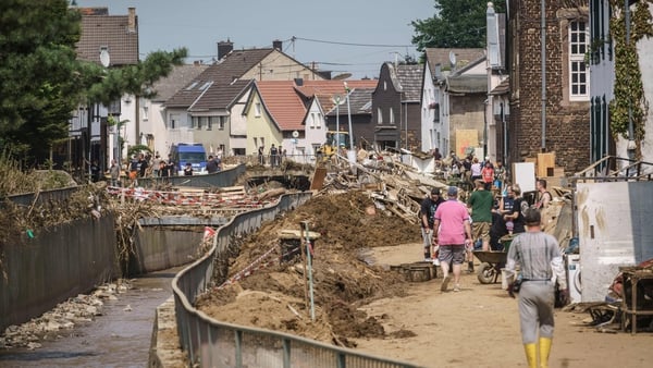 People walk on a muddy street along the river among piles of debris in Swisttal-Odendorf, near Euskirchen, North Rhine-Westphalia