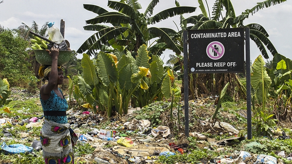 A woman walks past contaminated lands in Nigeria
