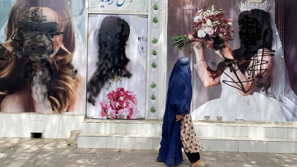 A woman passes by a beauty salon in Kabul, where photos of women have been covered in black pain