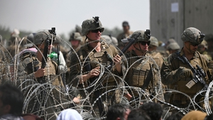 US soldiers stand guard as Afghans sit near the military part of the airport in Kabul