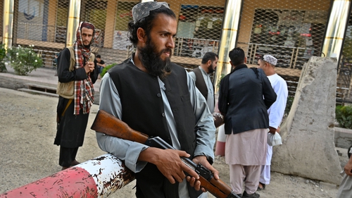 A Taliban fighter stands at a gate as people wait with their documents outside the passport office in Kabul