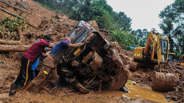 Rescue workers push a overturned vehicle stuck in the mud and debris at a site of a landslide in Kokkayar, India