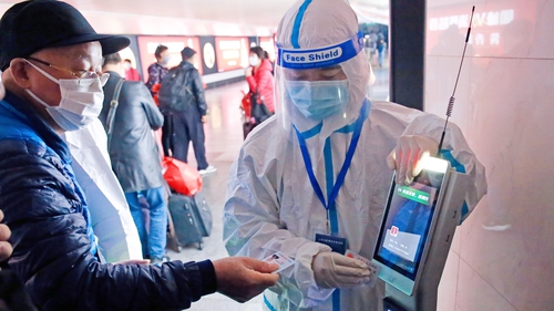 Workers in PPE check the travel history of arriving travellers at a railway station in Shanghai