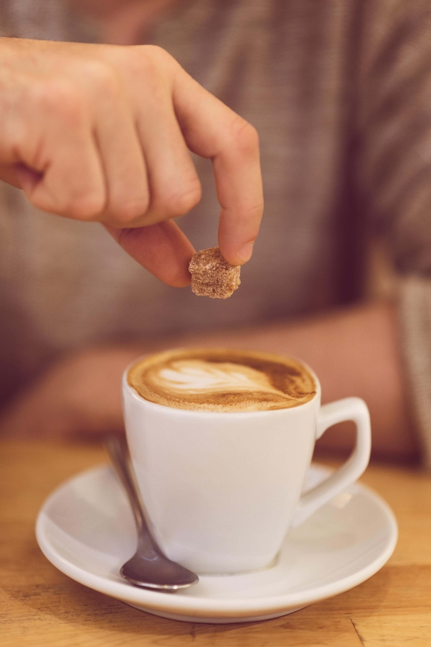 Hand putting sugar lump into coffee