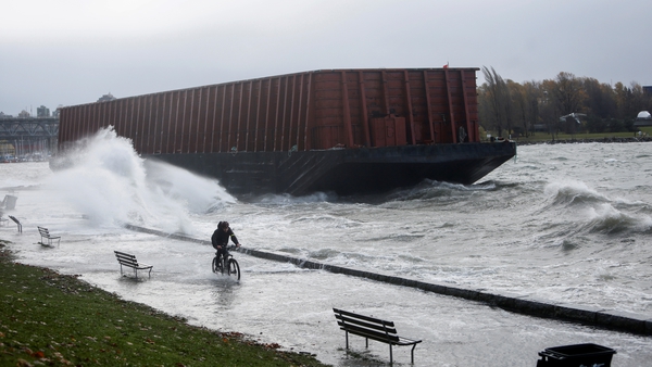 A man cycles along a sea wall past a barge that came loose from its moorings in Vancouver