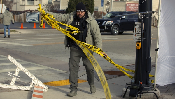 A police officer clears police tape at the scene in Waukesha today