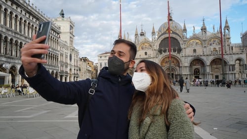 A couple wearing protective masks, takes a selfie in Piazza San Marco in Venice