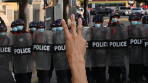 A protester holds up the three-finger salute as police block a street during a demonstration against the military coup