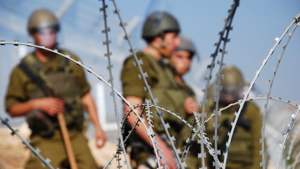 Four Israeli soldiers stand behind razor wire near the Palestinian village of Bil'in in the West Bank