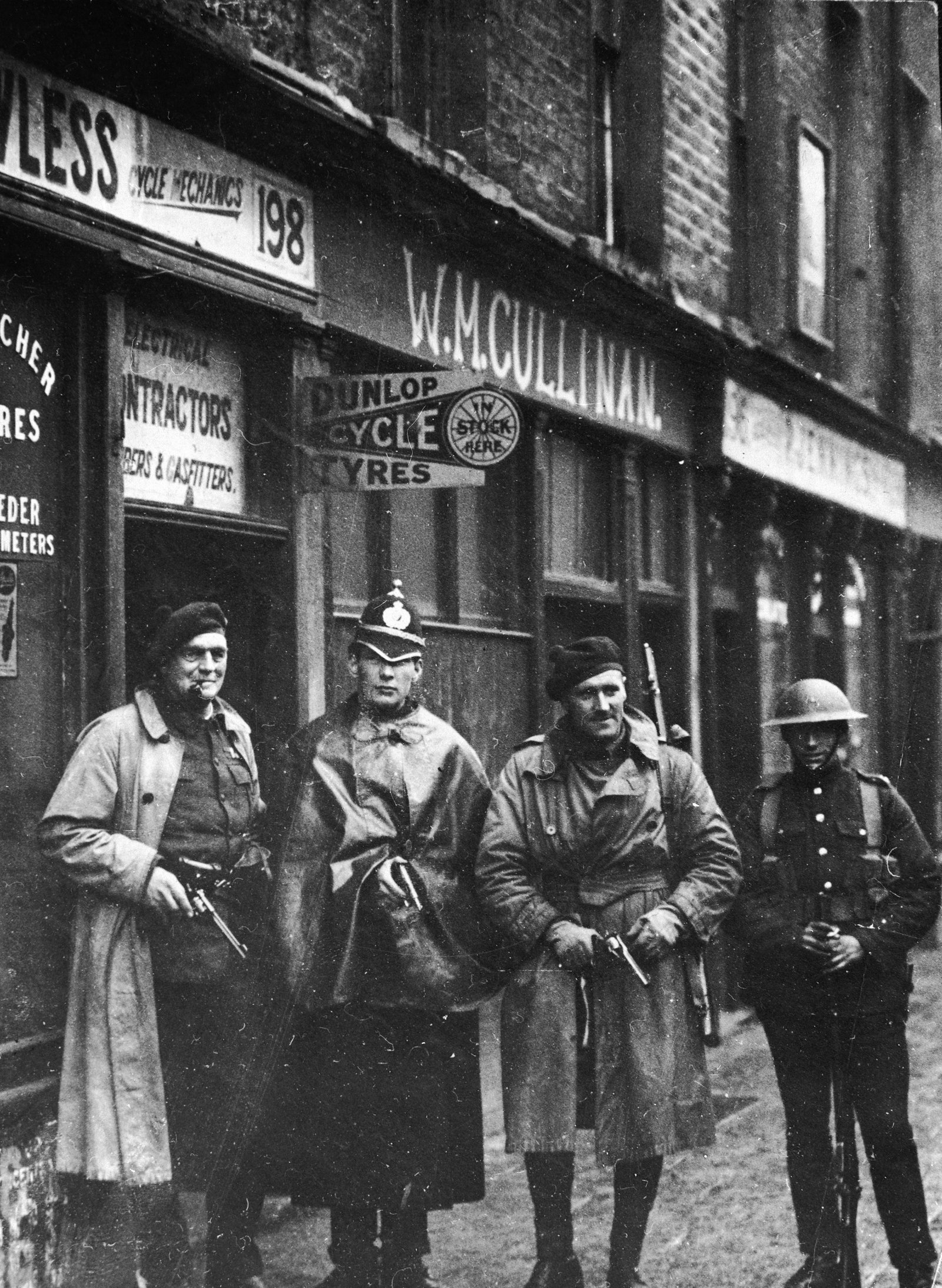 Image - Posed photo of two Auxiliaries, a DMP Constable, and a British soldier in Dublin. The DMP man sheepishly holds a pistol. In fact by October 1920, they had opted out of the war against the IRA. Image: Getty Images