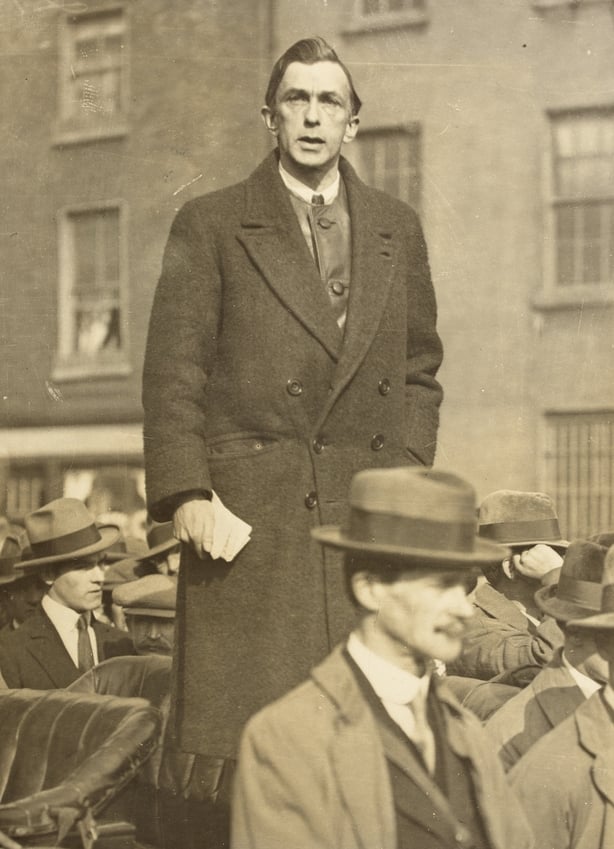 Sepia photo of man in coat giving a speech outdoors
